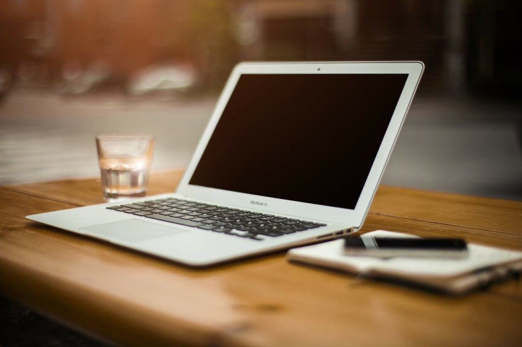 macbook cinza com a tela apagadaem cima de uma mesa de madeira