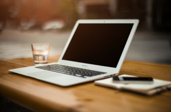 macbook cinza com a tela apagadaem cima de uma mesa de madeira