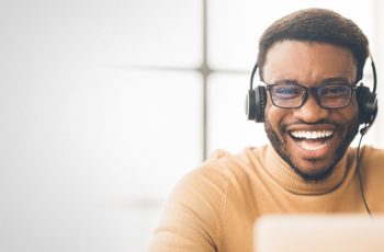homem negro de óculos sorrindo e utilizando um fone de ouvido com fio