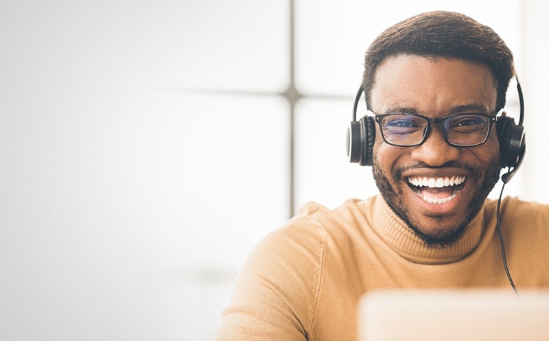 homem negro de óculos sorrindo e utilizando um fone de ouvido com fio