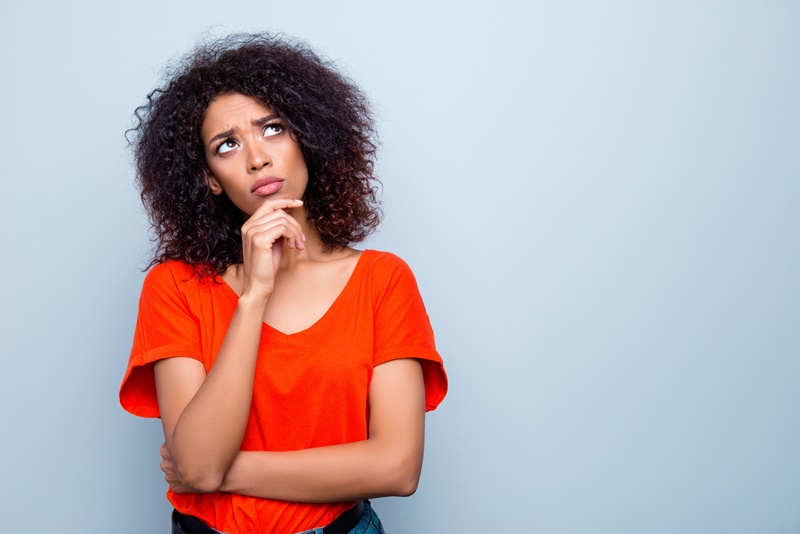 Mulher jovem, com cabelo cacheado, com expressão de dúvida