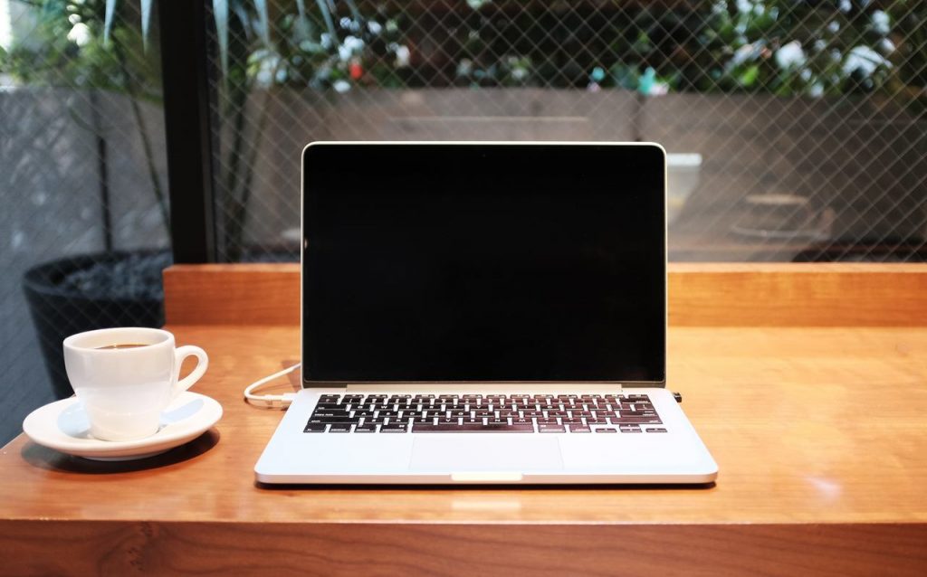 Notebook positivo com tela preta sobre mesa ao lado de uma xícara de café