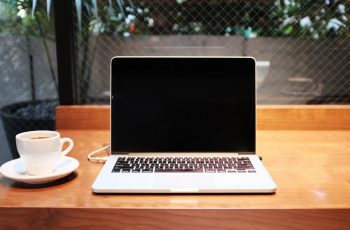 Notebook positivo com tela preta sobre mesa ao lado de uma xícara de café