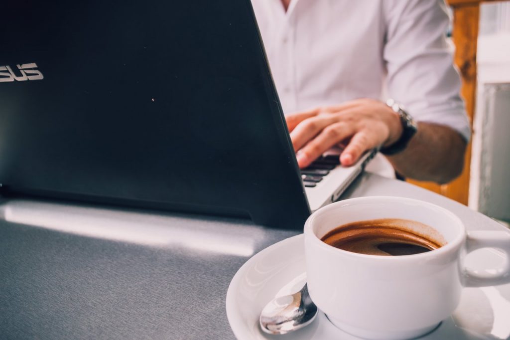 Homem utilizando laptop asus em uma mesa ao lado de uma xícara de café