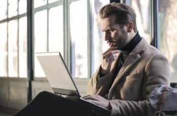 Homem com mão no queixo com um olhar perplexo sobre a tela do notebook que está de cabeça para baixo