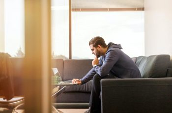 Homem sentado em um sofá com os dedos no teclado do notebook