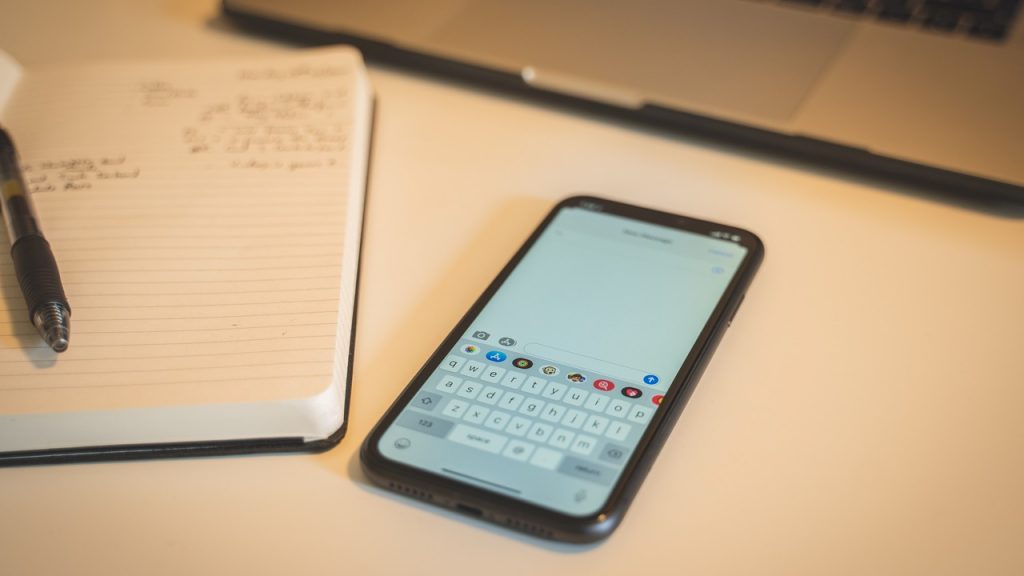 Iphone com teclado iphone em sua tela ao lado de um caderno em uma mesa