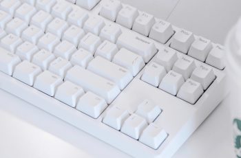 Teclado branco com teclas como Scroll lock ao lado de um copo de café