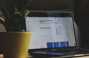 Notebook com tela escura ao lado de uma planta sobre uma mesa