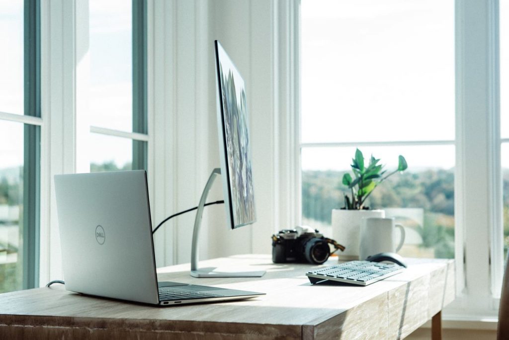 Notebook, teclado e mouse dell sobre mesa ao lado de uma janela