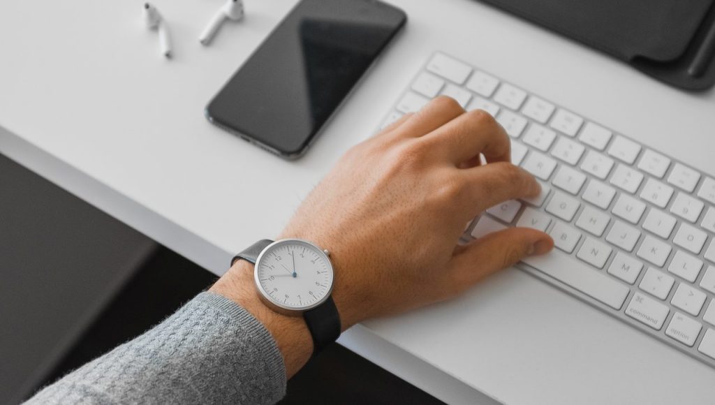 Homem com relógio na mão utilizando teclas do teclado para desligar pc