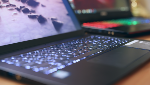 Notebook em primeiro plano com teclado iluminado com led branco, mais ao fundo outro notebook com o teclado iluminado com led colorido.