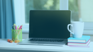 Notebook com tela preta em cima da mesa, ao lado de uma xícara, livros e canetas.