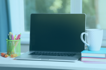 Notebook com tela preta em cima da mesa, ao lado de uma xícara, livros e canetas.