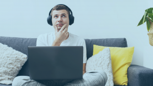 Homem com dúvida, sentando em um sofá e com um notebook sobre suas pernas