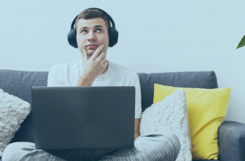 Homem com dúvida, sentando em um sofá e com um notebook sobre suas pernas