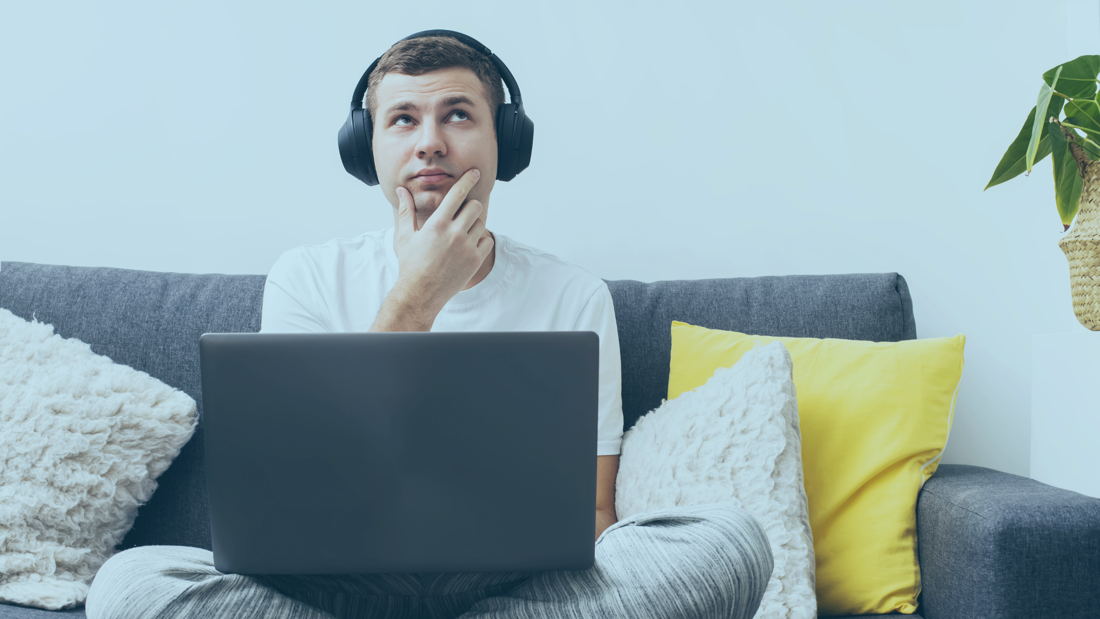 Homem com dúvida, sentando em um sofá e com um notebook sobre suas pernas