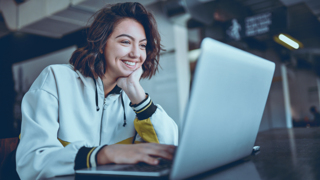 Mulher feliz sentada em uma mesa e estudando com seu notebook