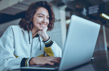 Mulher feliz sentada em uma mesa e estudando com seu notebook