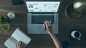 Mulher mexendo em seu notebook com uma xícara a caderno ao lado