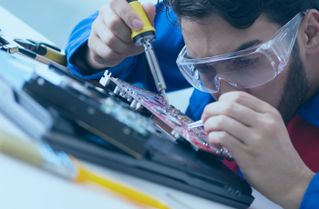 Técnico de informática apoiado sobre uma placa enquanto realiza uma manutenção.