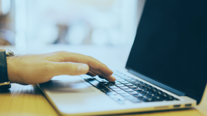 Homem com a mão pousada sobre um notebook.