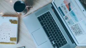 Notebook visto de cima, ao lado, uma xícara de café e uma agenda.