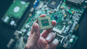Mão segurando um processador, ao fundo temos o restante da placa eletrônica
