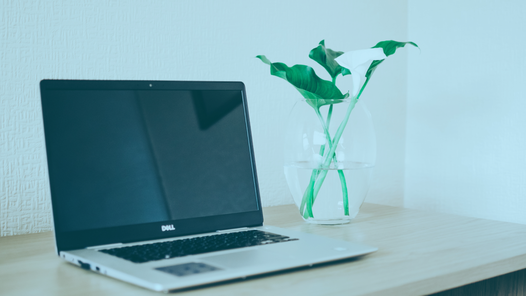 Imagem de um notebook Dell sobre a mesa. Ao fundo, um vaso de flores.